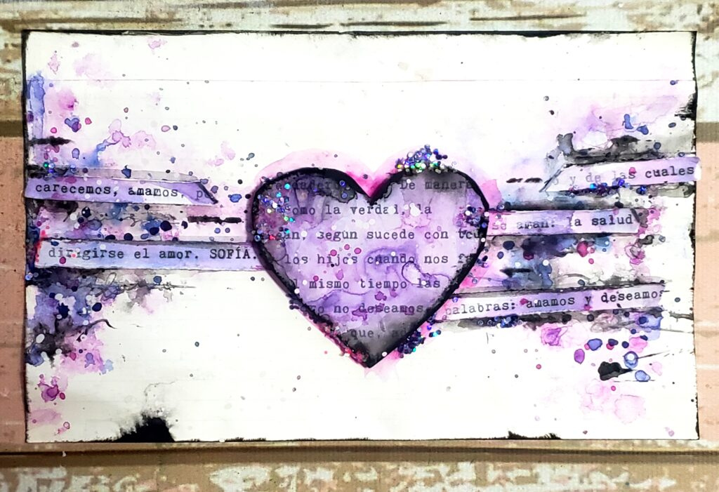 En la imagen se vé una hoja de Art Journal de composición horizontal doble triangulo con forma de moño, donde el centro está ocupado con un corazón violeta y enmarcado en negro, se ven brillos de glitter y palabras que aluden a los hijos. 