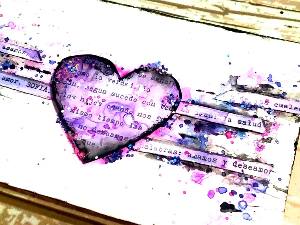 En la imagen se vé una hoja de Art Journal de composición horizontal doble triangulo con forma de moño, donde el centro está ocupado con un corazón violeta y enmarcado en negro, se ven brillos de glitter y palabras que aluden a los hijos. 